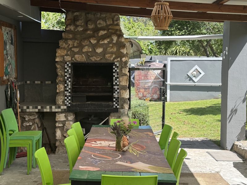 Covered outdoor patio featuring a rustic stone fireplace, tiled flooring, and timber roof beams, overlooking a private garden area.