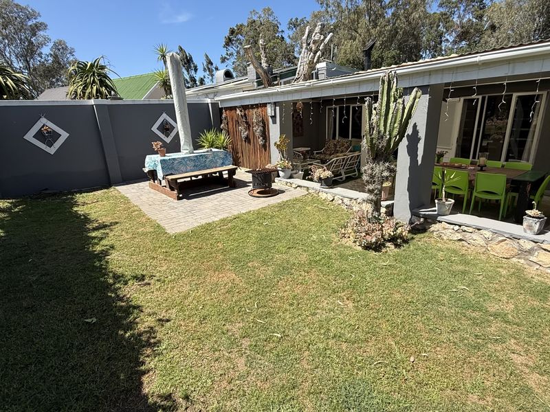 A rear garden featuring a paved patio area, a stone retaining wall, and a covered veranda attached to the main house structure.