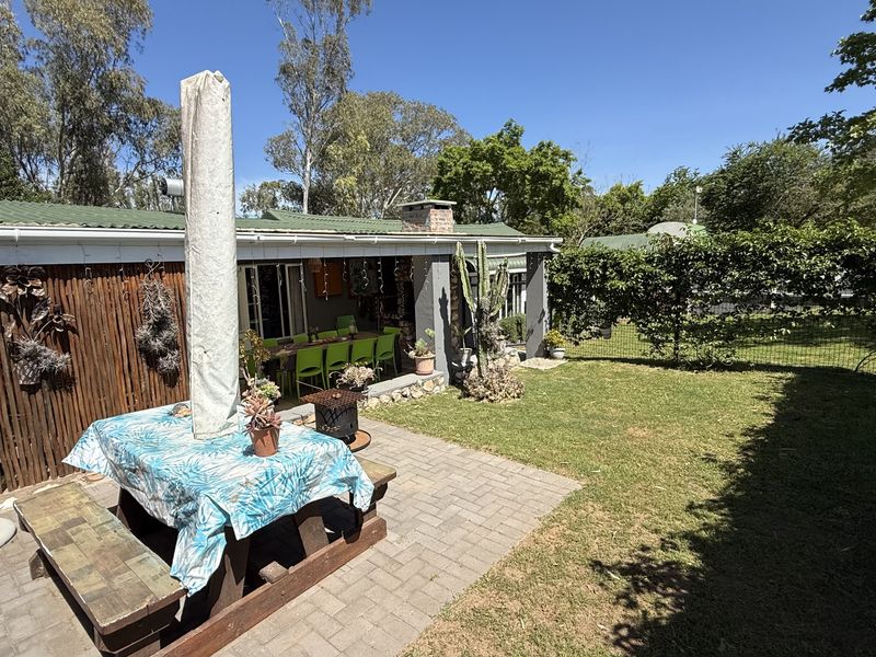 A rear garden view featuring a paved patio area, a covered veranda, and a well-maintained lawn with established perimeter fencing.