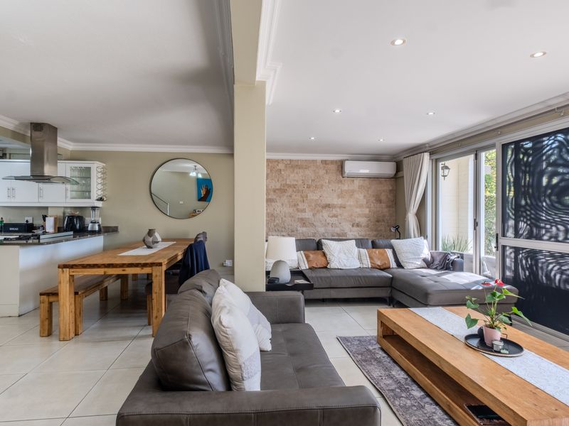 Spacious open-plan living and dining area featuring a stone accent wall, modern kitchen with stainless steel extractor, and large sliding doors leading to the patio.