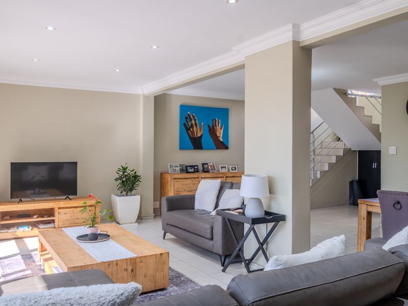 Spacious open-plan living area featuring neutral walls, recessed lighting, crown molding, and tiled flooring, with an adjacent staircase leading to the upper level.
