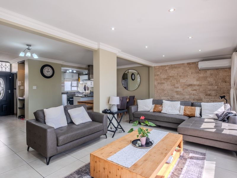 Spacious open-plan living area featuring tiled floors, a stone accent wall, recessed lighting, and an integrated air conditioning unit, seamlessly connecting to the kitchen.