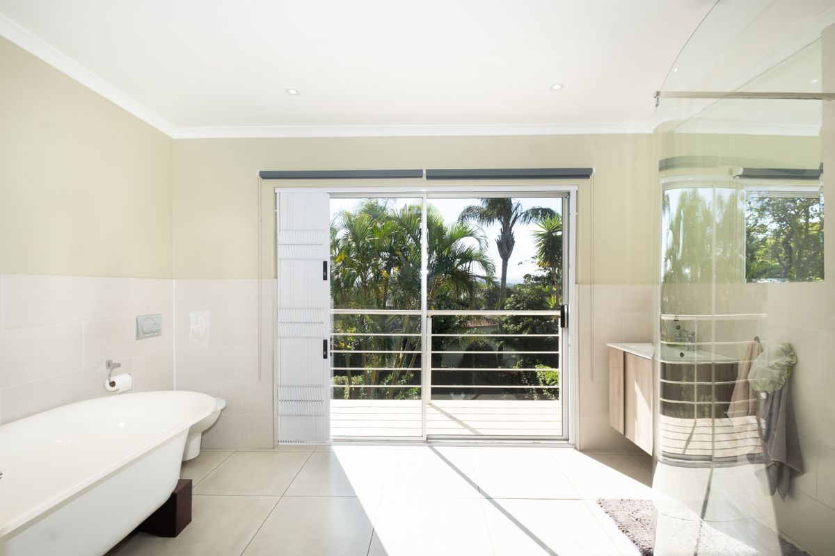 A bright, modern bathroom featuring a freestanding bathtub, a curved glass shower, and sliding doors opening to an outdoor balcony area.