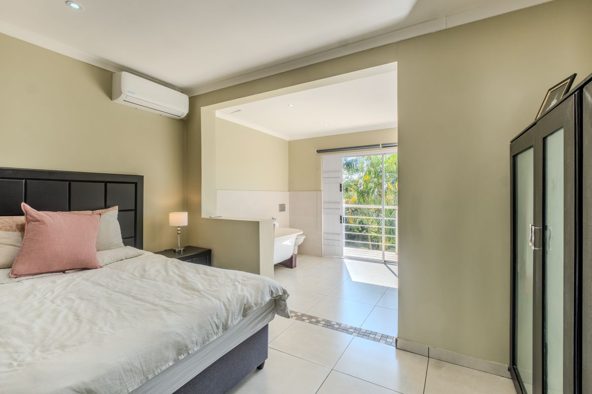 Spacious bedroom featuring an open-plan ensuite area with a freestanding bathtub, tiled flooring, and direct access to a private balcony through sliding glass doors.