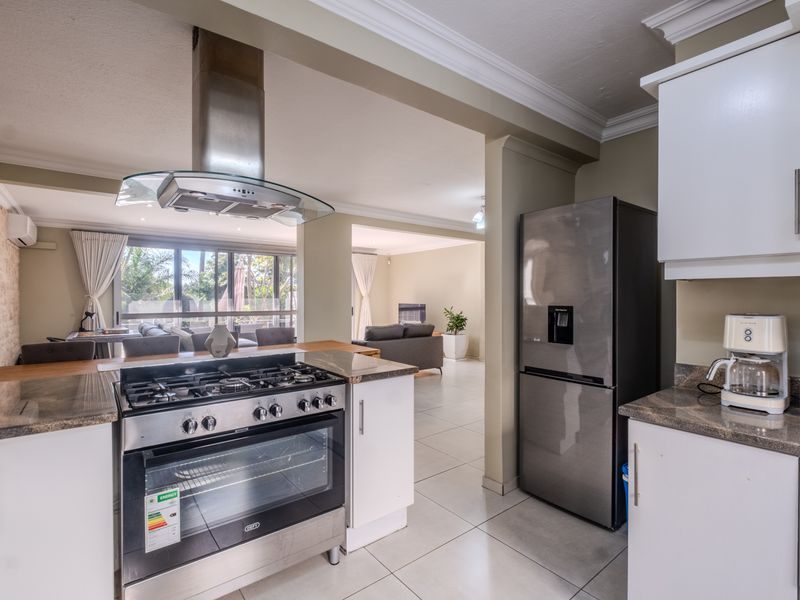 Open-plan kitchen featuring granite countertops, gas stove, and extractor fan, flowing seamlessly into a spacious living area with large sliding doors to the patio.