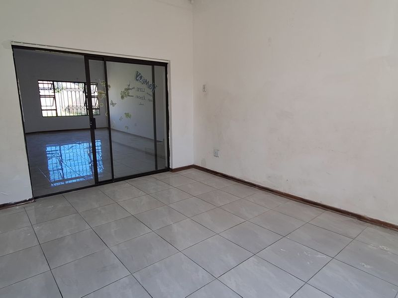An empty living room featuring tiled flooring and a sliding glass door leading to an adjacent space with security bars.