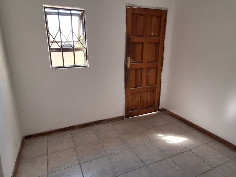 A functional laundry area featuring tiled flooring, a wall-mounted water tap, and a secure timber door with a security gate.