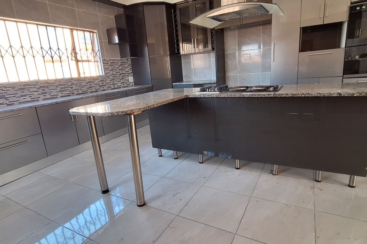 Modern kitchen featuring granite countertops, built-in oven, gas hob, extractor fan, and ample cabinetry, finished with tiled flooring and security bars on windows.
