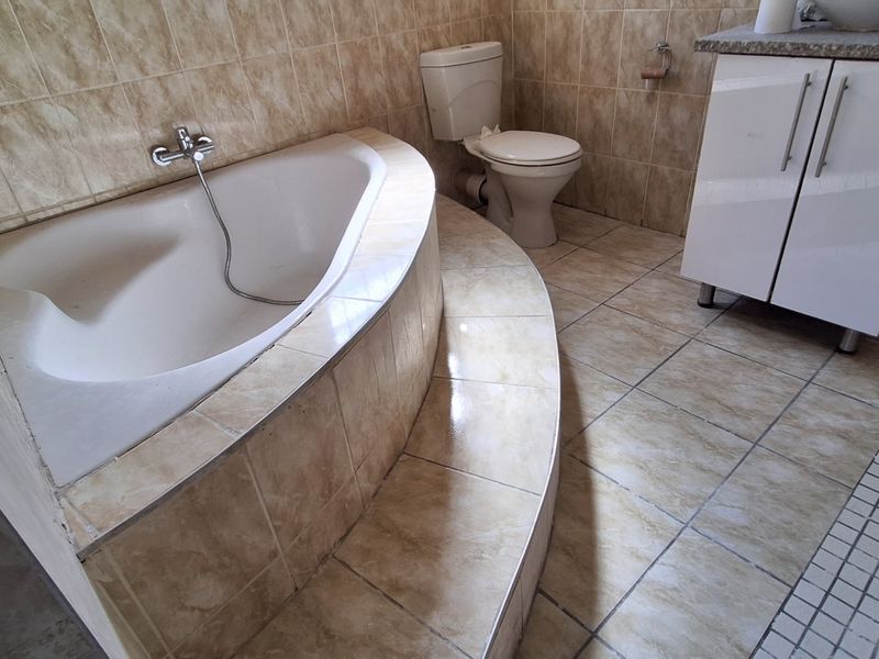 A bathroom featuring a raised built-in bathtub, a toilet, and a vanity cabinet with tiled walls and flooring.