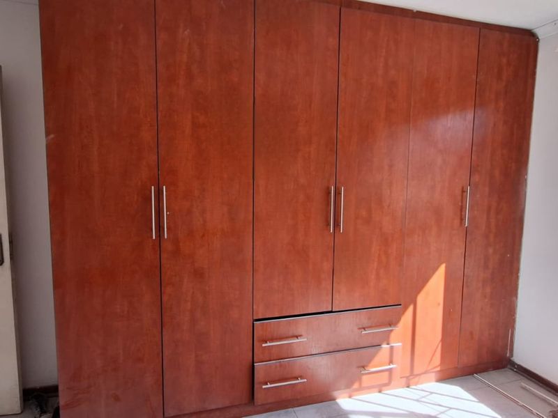 A bedroom featuring extensive built-in wooden cupboards, a security gate, and windows fitted with burglar bars.