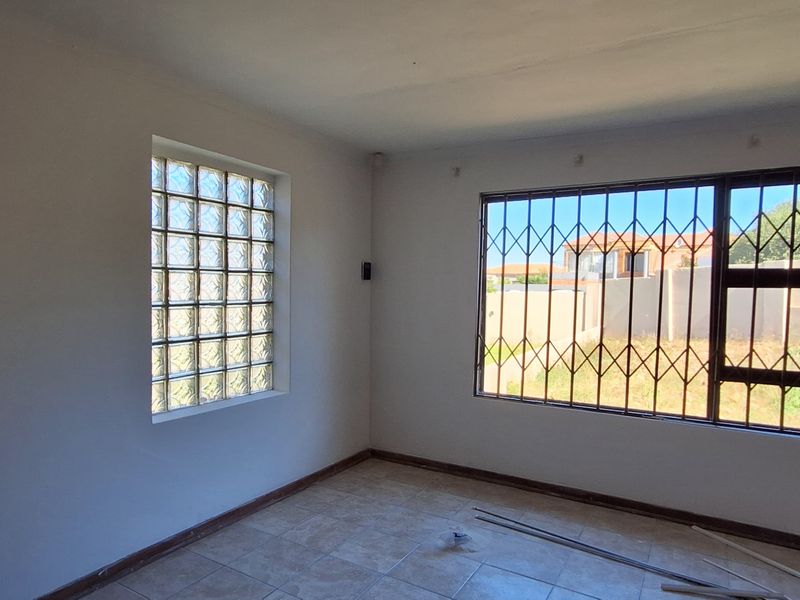 An empty living room featuring tiled flooring, a glass block window, and security bars on the main window.
