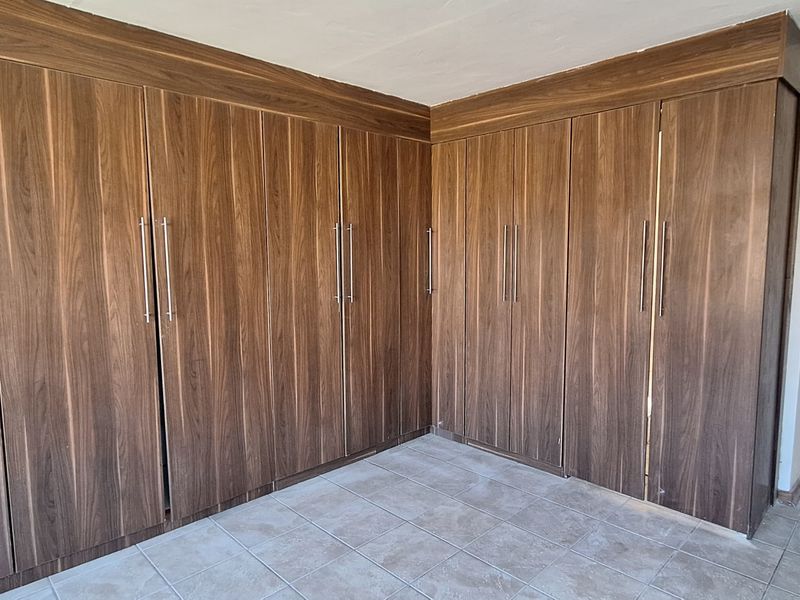A clean, empty bedroom featuring extensive floor-to-ceiling built-in wooden cupboards and neutral tiled flooring.