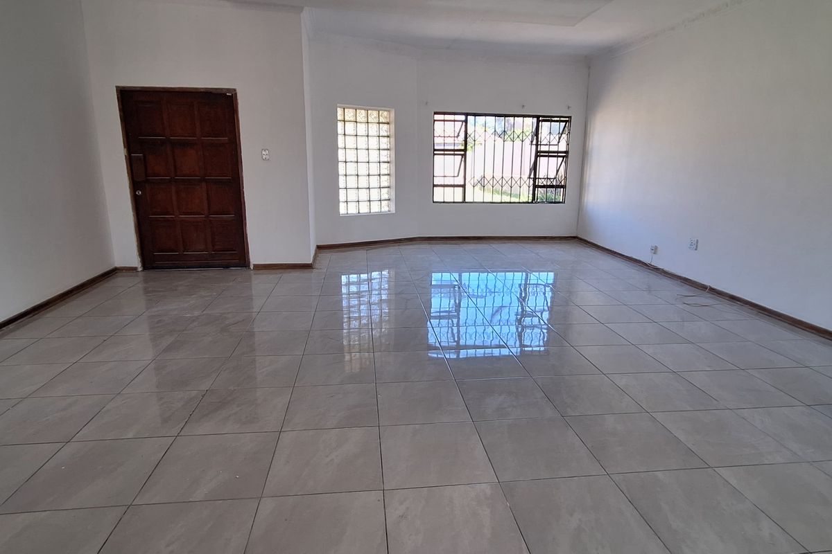 A spacious, empty living area featuring neutral tiled flooring, a timber entrance door, and a combination of glass block and standard security-barred windows.