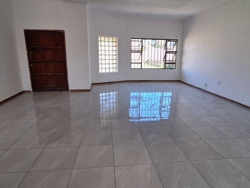 A spacious, empty living area featuring neutral tiled flooring, a timber entrance door, and a combination of glass block and standard security-barred windows.