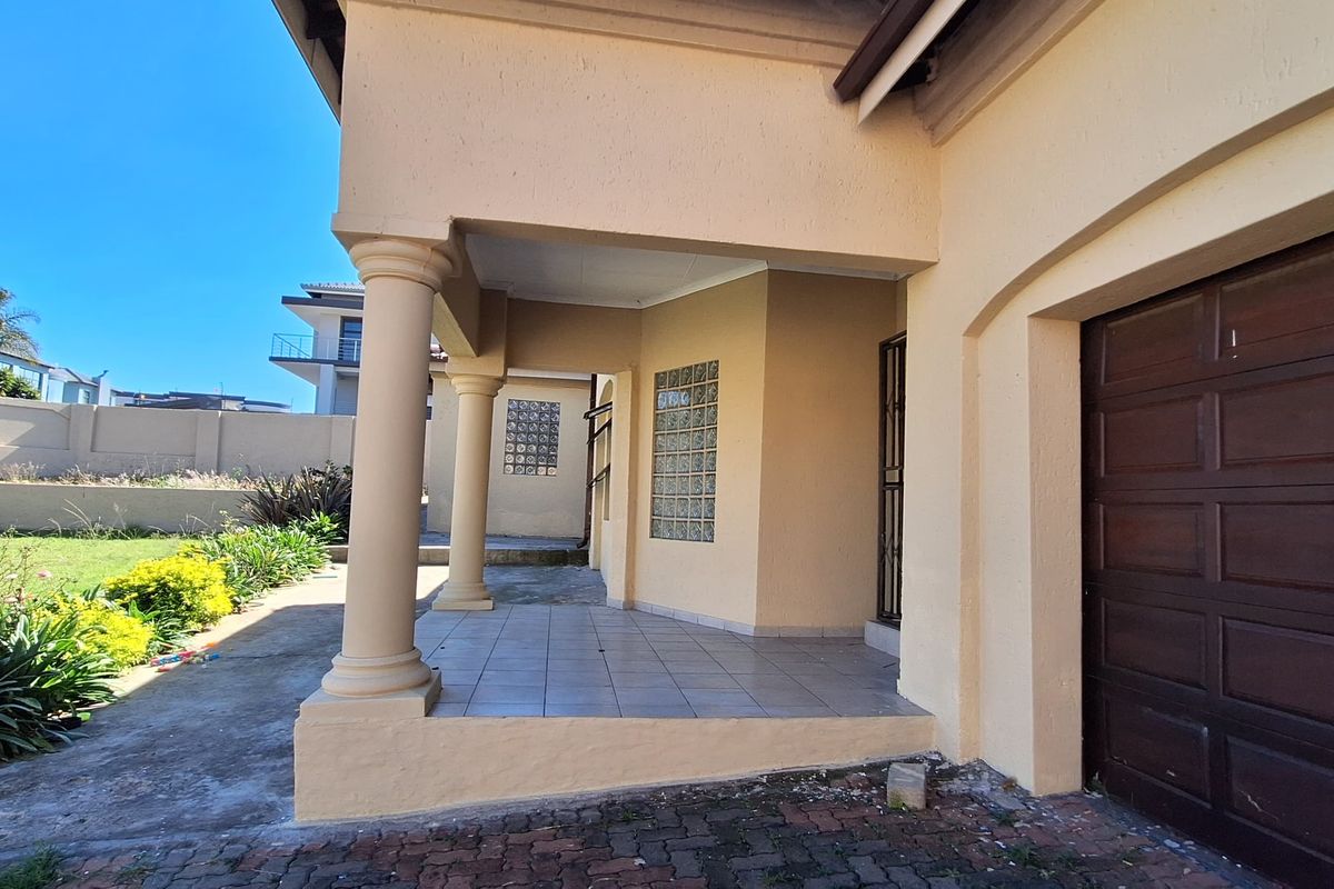 Rear exterior view featuring a covered tiled patio with concrete columns, glass block windows, and a sectional garage door opening onto a paved area.