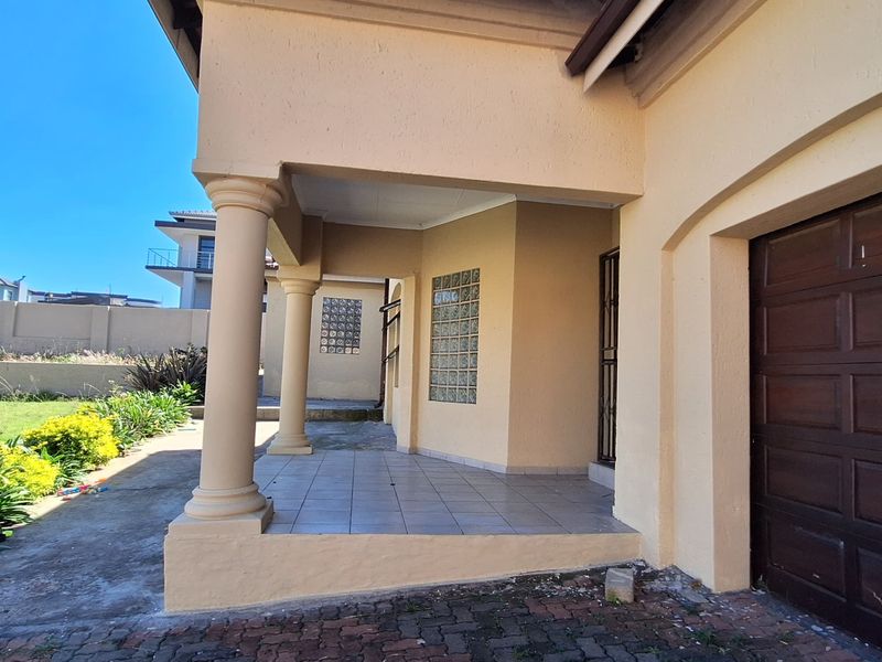 Rear exterior view featuring a covered tiled patio with concrete columns, glass block windows, and a sectional garage door opening onto a paved area.