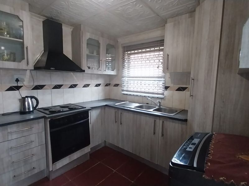 A functional kitchen featuring wood-look cabinetry, built-in oven and stove, extractor fan, and double sink with tiled backsplash.