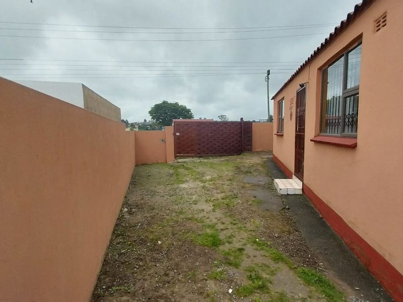 Rear exterior area featuring a perimeter boundary wall, metal security gate, and access to the main dwelling with security bars on windows.