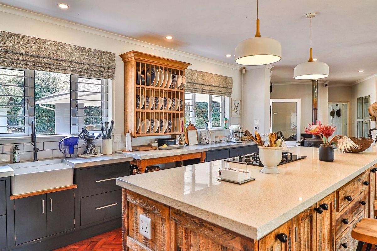 A well-appointed kitchen featuring a large stone island, farmhouse sink, gas hob, and a mix of modern dark cabinetry with rustic timber accents.