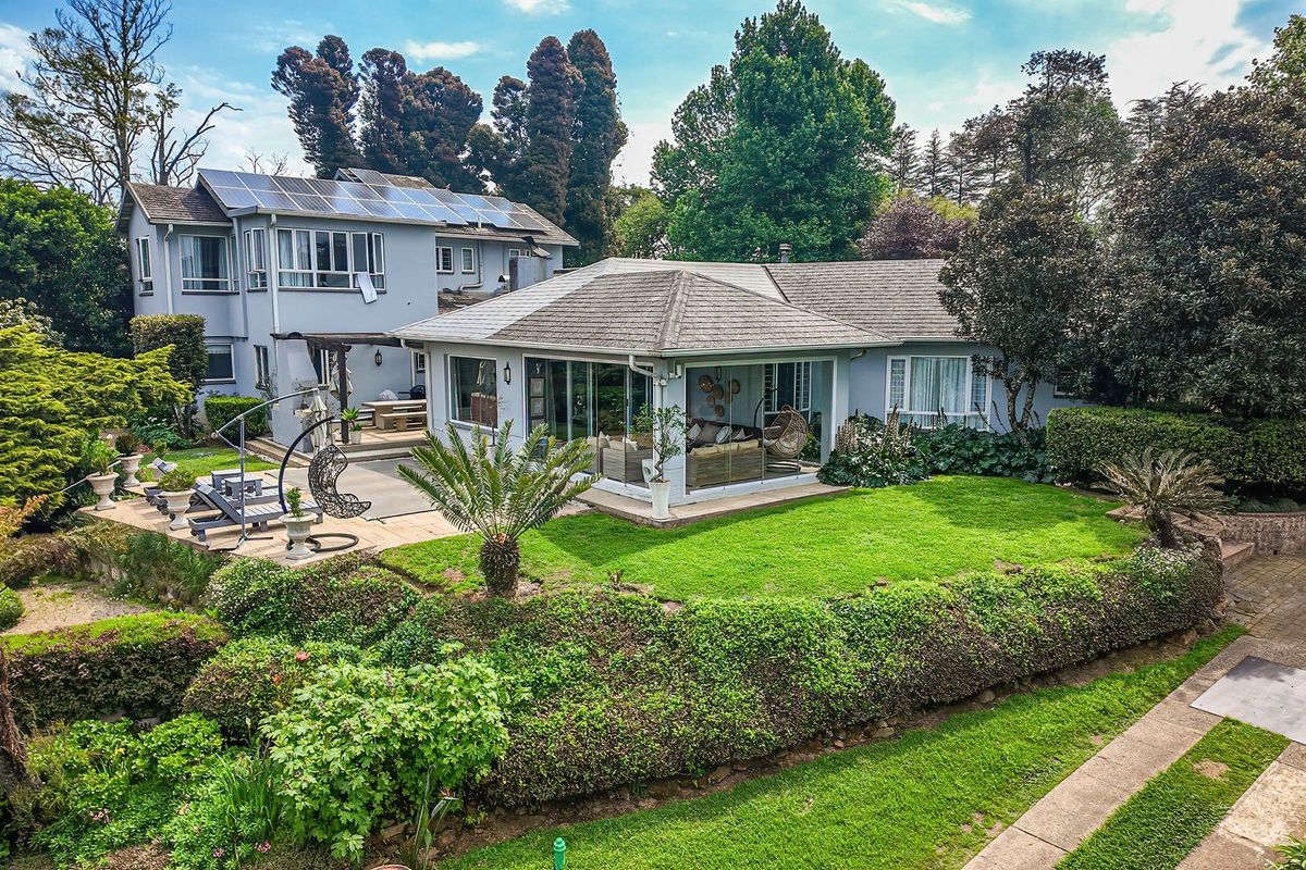 Aerial view of the rear elevation featuring a well-maintained garden, paved patio area, and a multi-level house with solar panels installed on the roof.