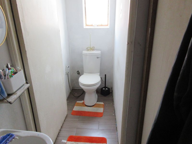 A compact bathroom featuring a standard toilet, bidet spray, and tiled flooring, requiring cosmetic updates to the walls and finishes.
