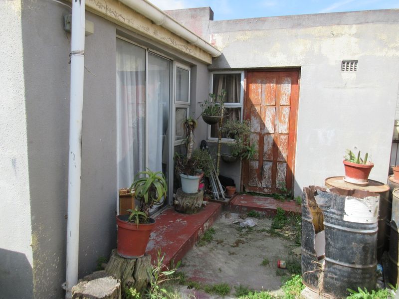 Rear exterior view showing a weathered timber door, sliding glass door, and concrete threshold area in need of maintenance and refurbishment.
