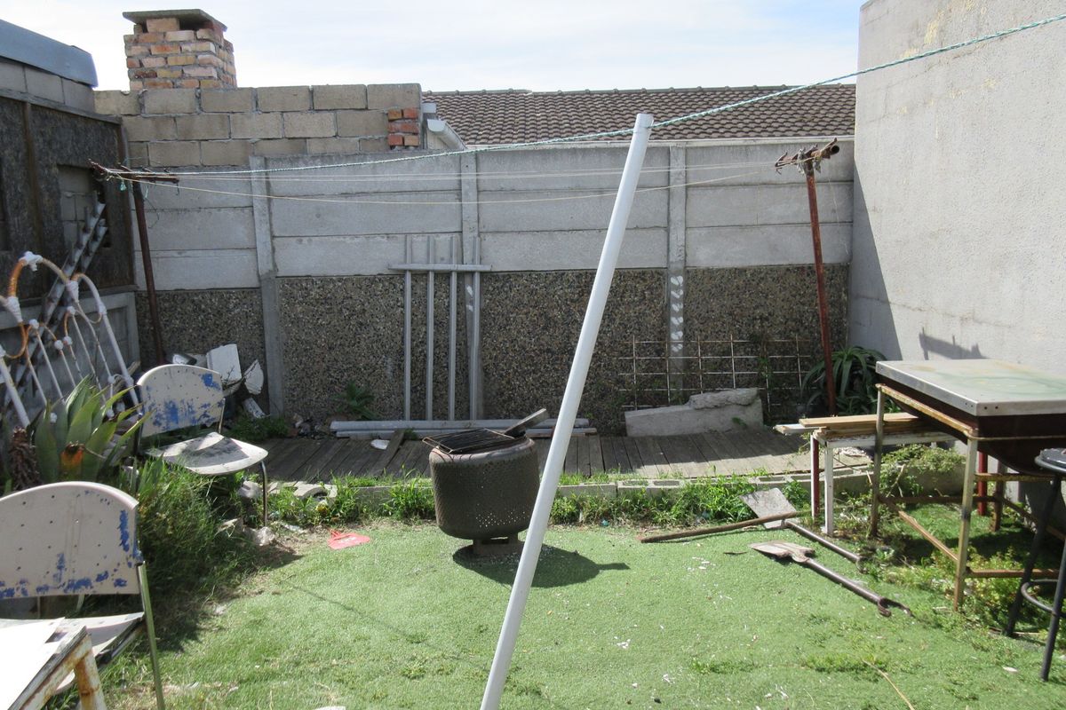 A rear outdoor area featuring a precast concrete boundary wall, timber decking, and artificial lawn, requiring landscaping and maintenance to improve its overall appeal.