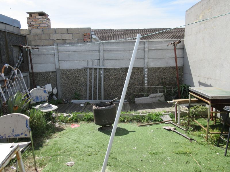A rear outdoor area featuring a precast concrete boundary wall, timber decking, and artificial lawn, requiring landscaping and maintenance to improve its overall appeal.