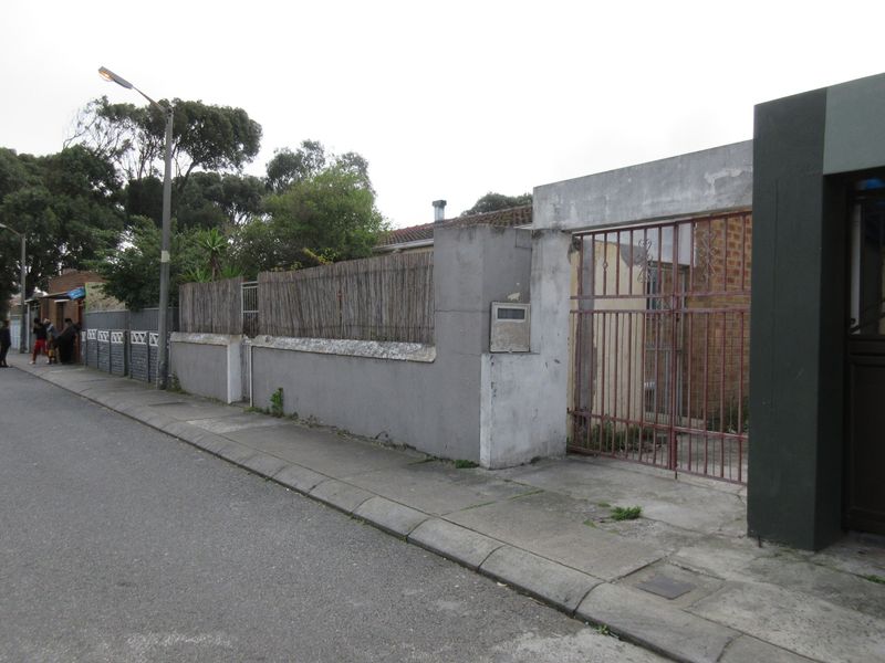 Street view of the property frontage featuring a perimeter wall, metal gate, and sidewalk access.