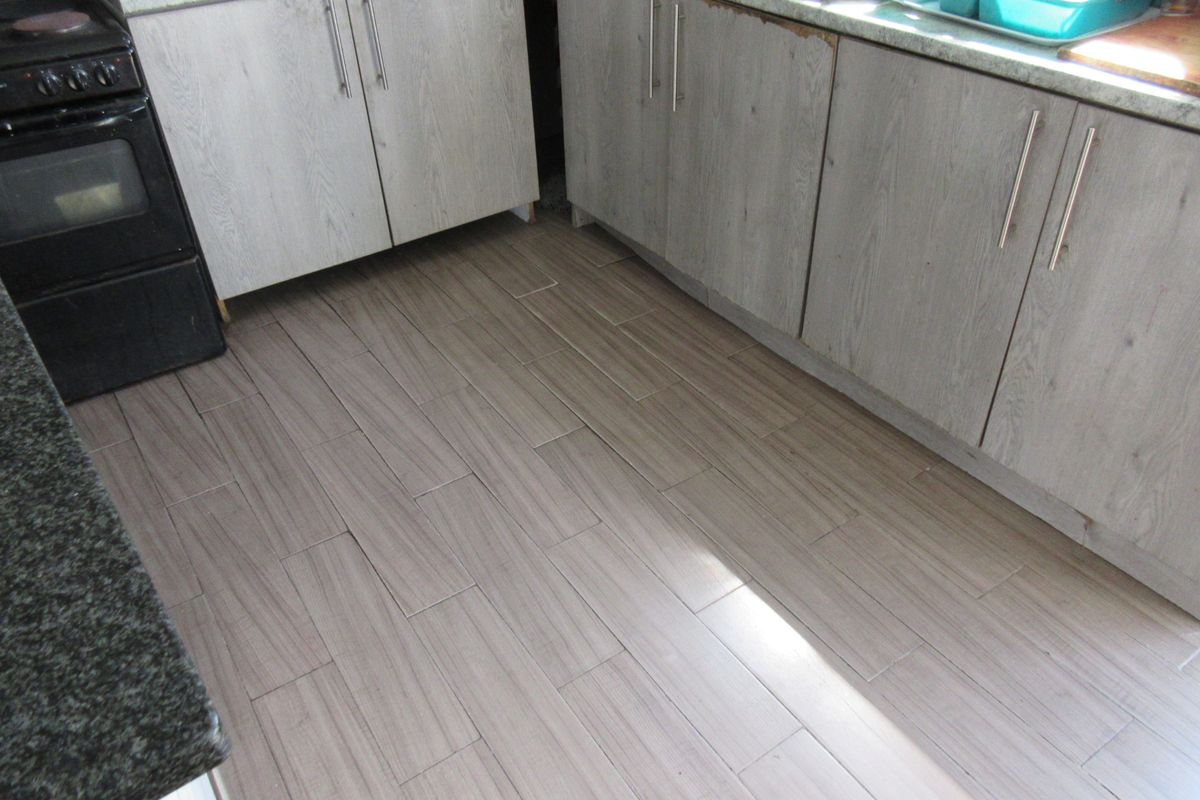A kitchen area featuring wood-look cabinetry, stone countertops, and tiled flooring, showing signs of wear on the cabinet edges and floor installation.