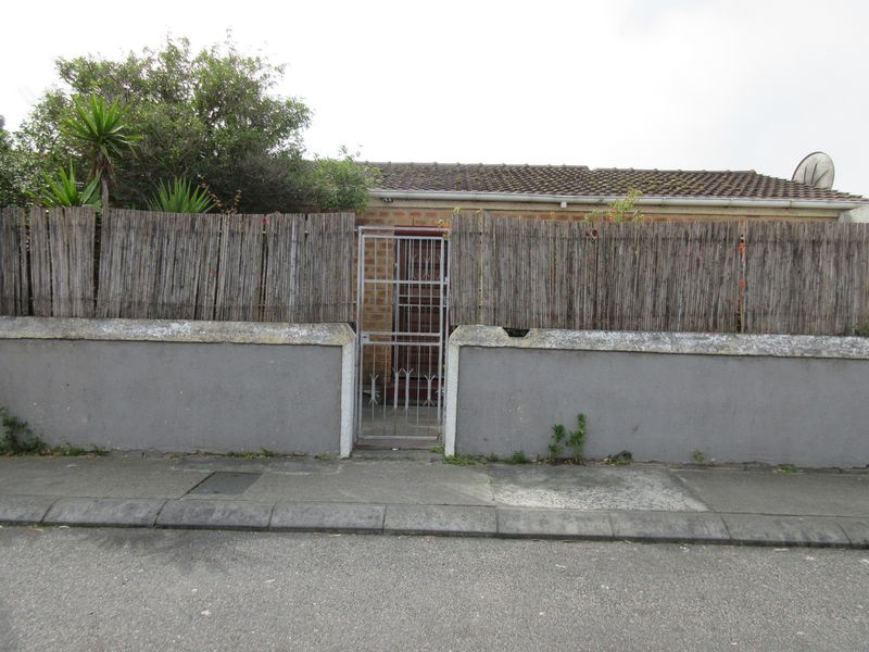 Front view of the property featuring a brick facade, tiled roof, and a secure gated entrance behind a boundary wall.