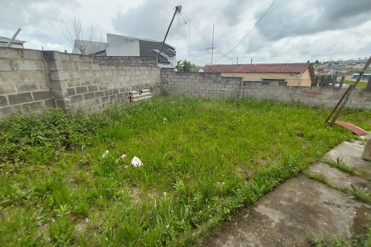 A rear garden area featuring a concrete block boundary wall and paved section, currently requiring significant landscaping and maintenance.