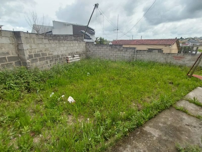 A rear garden area featuring a concrete block boundary wall and paved section, currently requiring significant landscaping and maintenance.