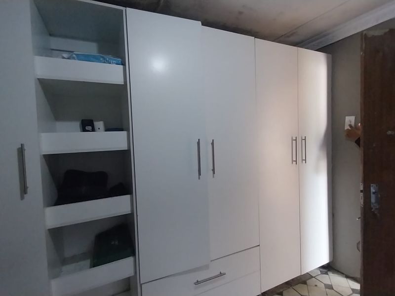A bedroom featuring white built-in cupboards and tiled flooring, showing visible signs of ceiling water damage requiring repair.