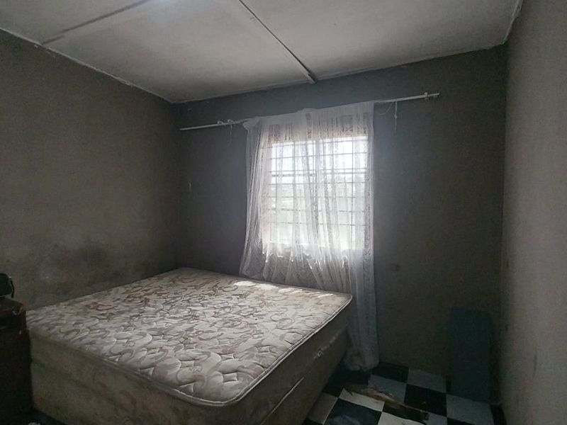 A bedroom featuring tiled flooring and security bars on the window, currently showing signs of wear and requiring maintenance to the walls and ceiling.