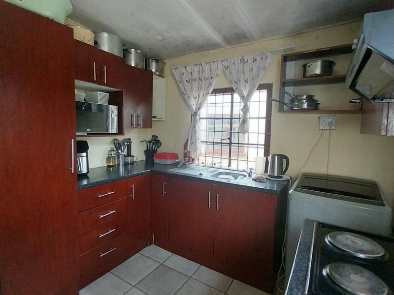 A functional kitchen featuring dark wood cabinetry, laminate countertops, a stainless steel sink, and an extractor fan, with tiled flooring throughout.