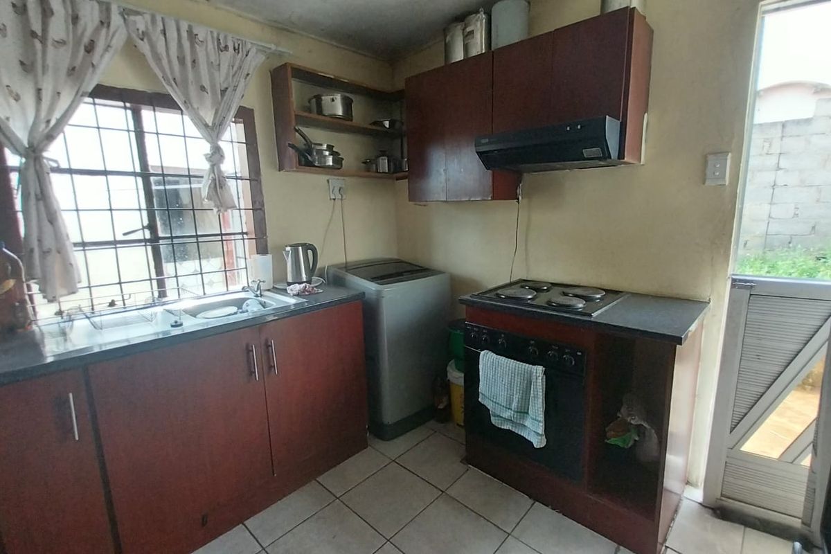 Compact kitchen featuring built-in cabinetry, an electric hob, oven, extractor fan, and tiled flooring with direct access to the exterior.