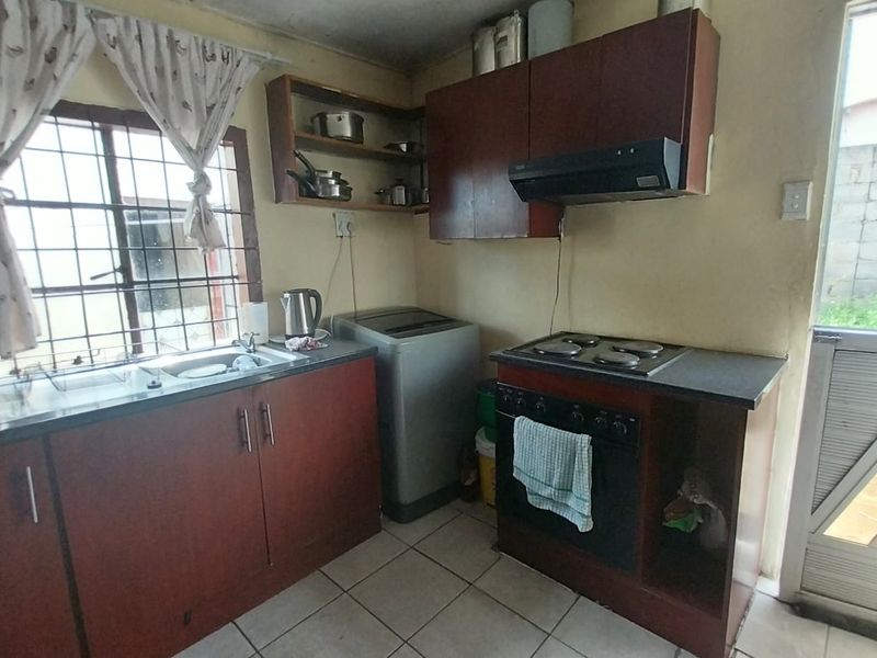 Compact kitchen featuring built-in cabinetry, an electric hob, oven, extractor fan, and tiled flooring with direct access to the exterior.