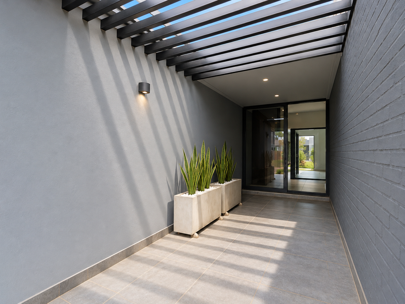 Modern covered entrance walkway featuring a sleek pergola, tiled flooring, and contemporary lighting leading to a glass-panelled front door.