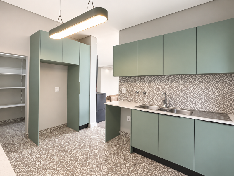 Modern scullery featuring sage green cabinetry, patterned tile flooring and backsplash, double sink, and an integrated walk-in pantry area.