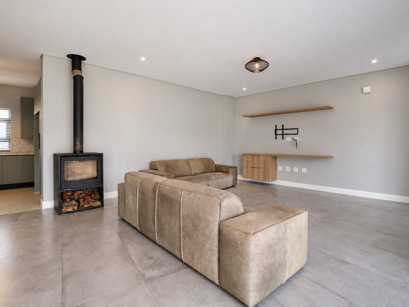 Modern open-plan living area featuring large format floor tiles, a sleek freestanding fireplace, and minimalist built-in shelving, seamlessly connecting to a contemporary kitchen space.