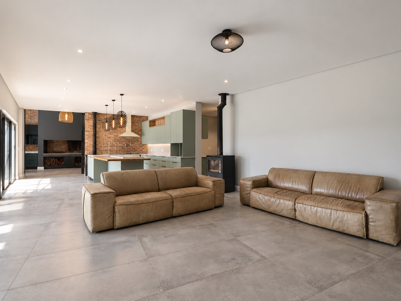 Spacious open-plan living and kitchen area featuring modern cabinetry, a central island, exposed brick accents, and a built-in fireplace with large sliding glass doors.