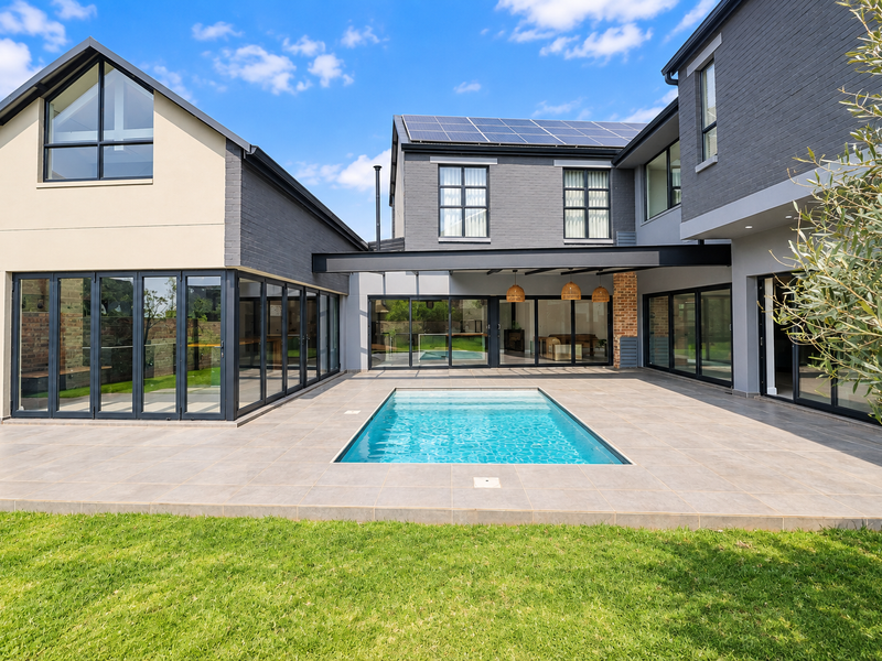 Modern rear exterior featuring a swimming pool, expansive tiled patio, and large bi-fold doors connecting the indoor and outdoor living spaces.