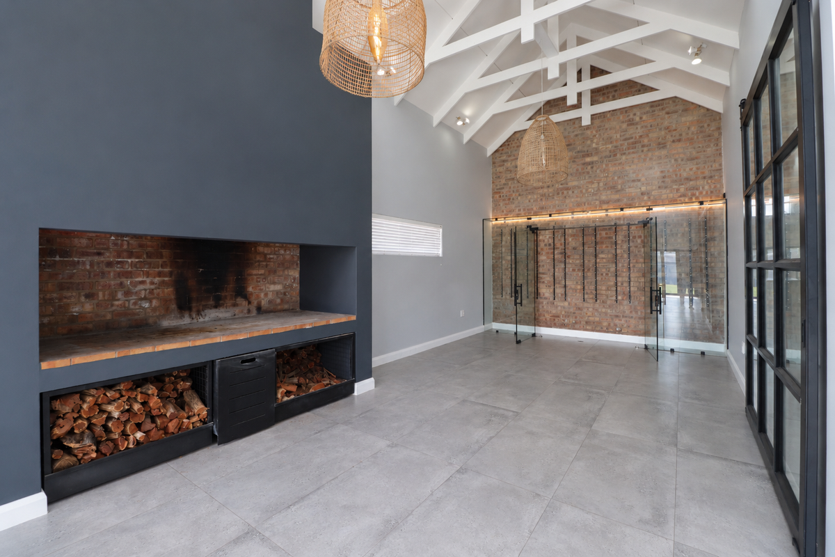 Spacious living area featuring a vaulted ceiling with exposed trusses, a built-in brick fireplace, and a modern glass-enclosed wine cellar.