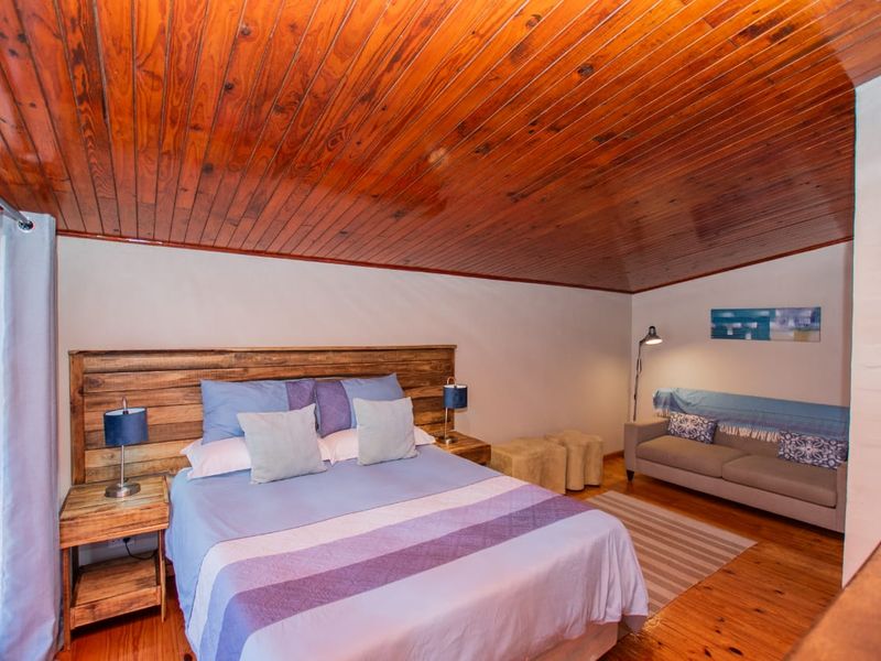A cozy bedroom featuring a warm timber tongue and groove ceiling, polished timber flooring, and a painted brick wall finish.