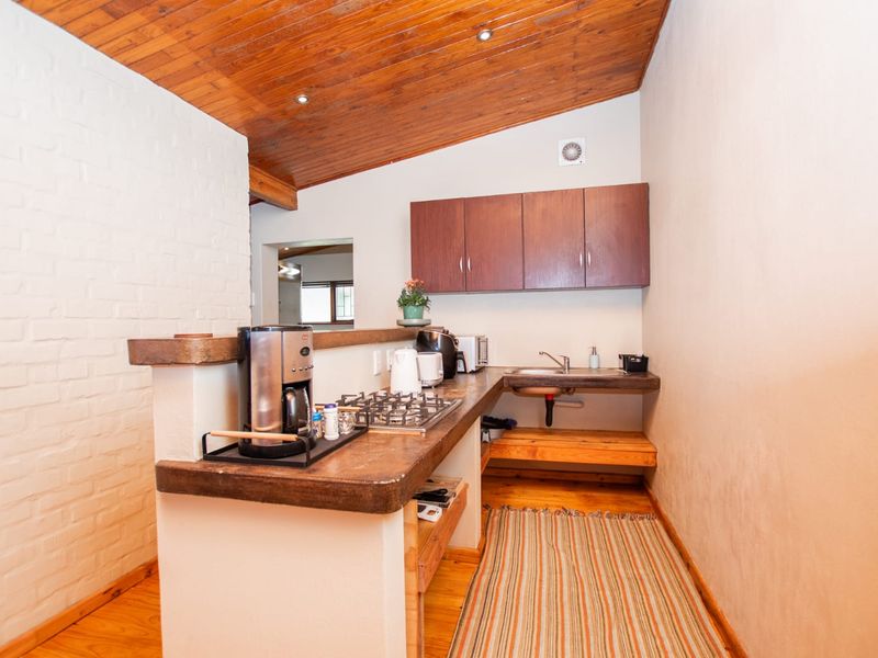 A compact kitchen featuring a built-in gas hob, stainless steel sink, timber ceiling, and exposed brick wall, offering a rustic cottage aesthetic.