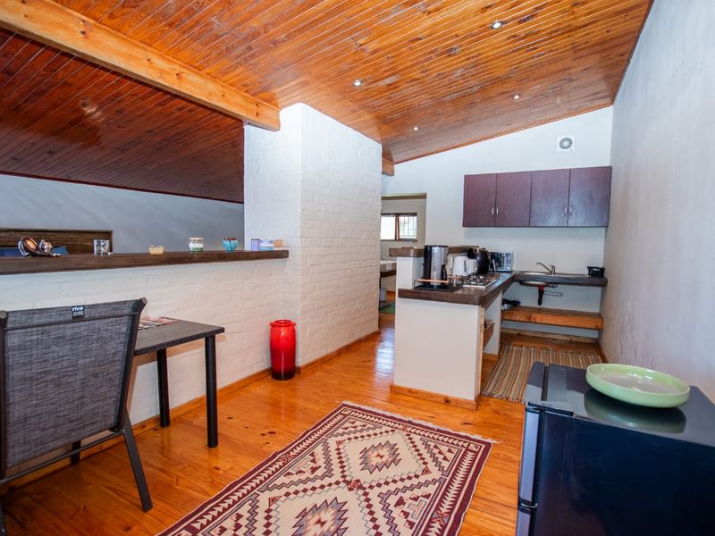 Open plan living and kitchen area featuring timber tongue and groove ceilings, exposed beams, timber flooring, and a functional kitchenette with built-in cabinetry.