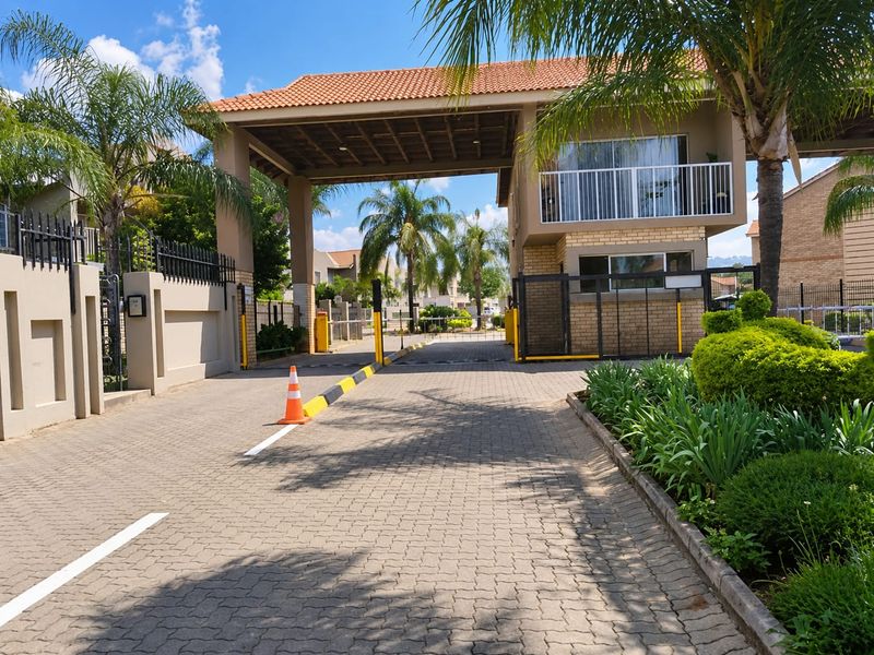 The entrance to the apartment complex features a secure gated access point with a guard house and paved driveway.