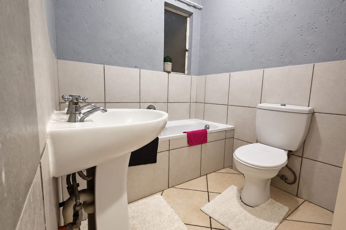 A functional bathroom featuring a pedestal basin, bathtub, and toilet with neutral wall and floor tiling.