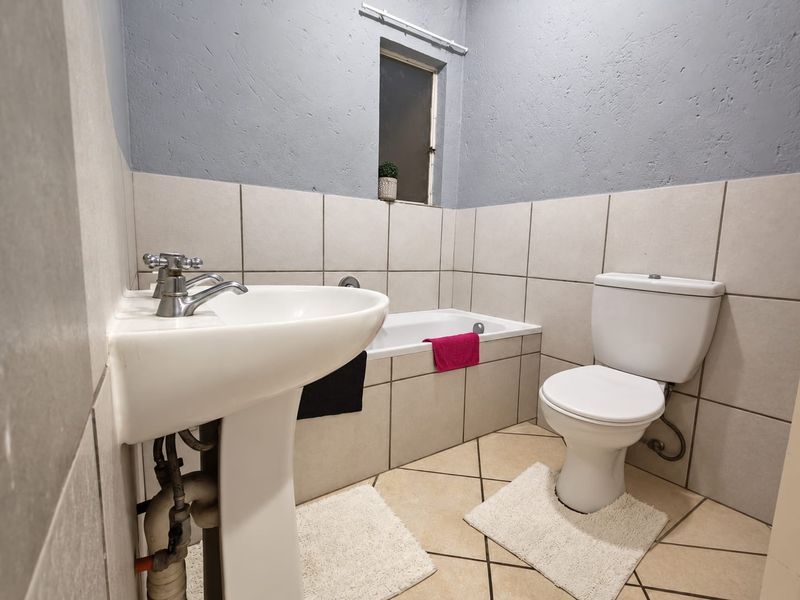 A functional bathroom featuring a pedestal basin, bathtub, and toilet with neutral wall and floor tiling.